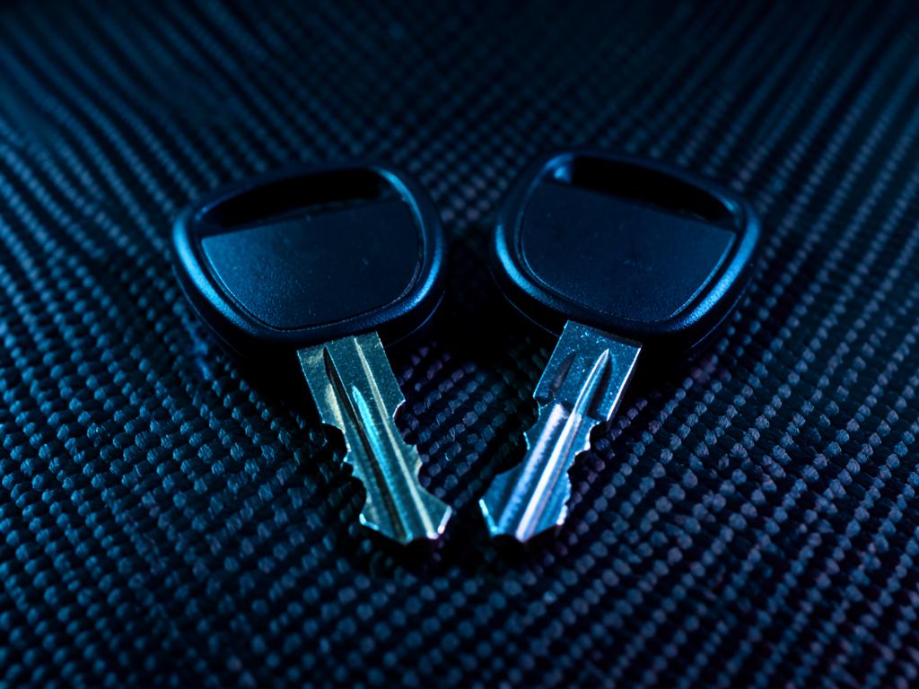 Two matching cut car keys on a dark carbon surface